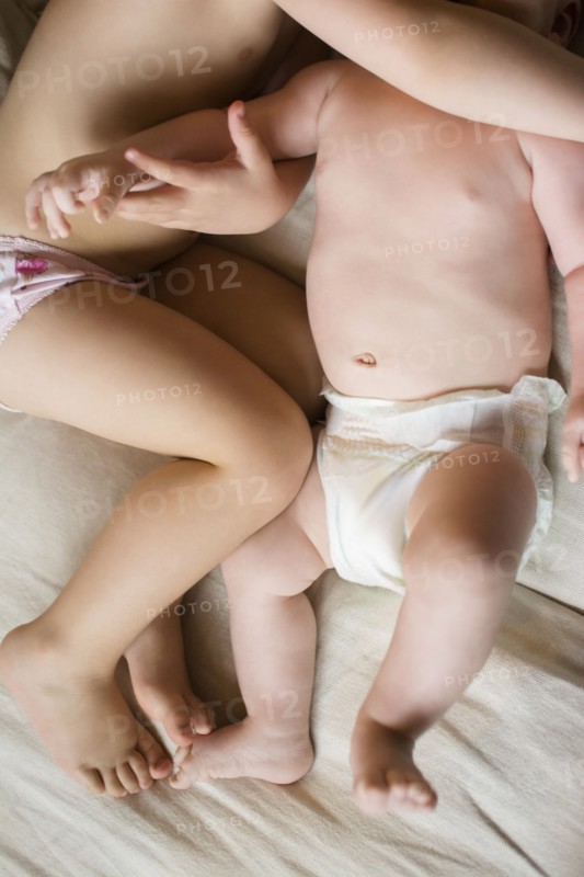 Girl (2-3) lying on bed with baby brother (6-11 months)