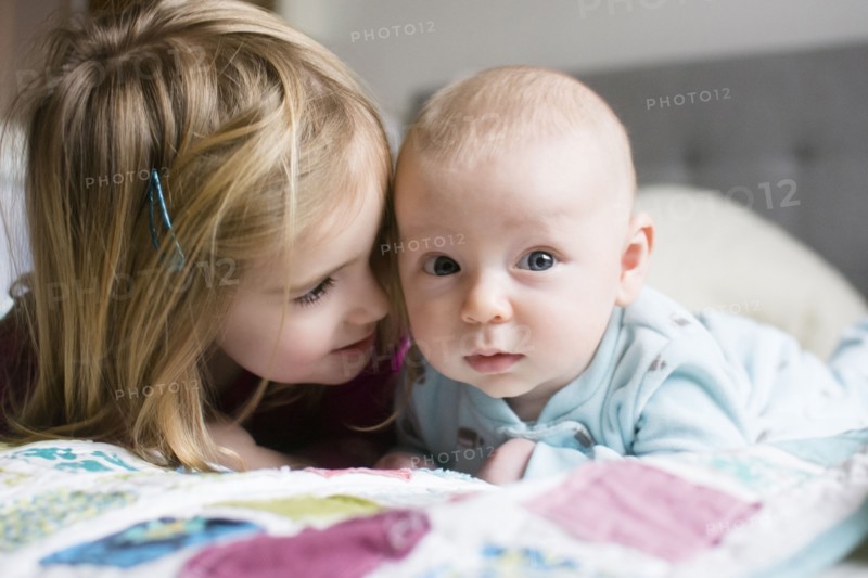Sister (2-3) and brother (6-11 months) lying on bed