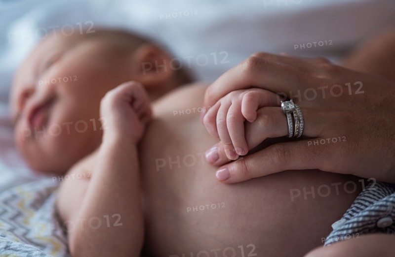 Mother holding son's (0-1 months) hand in bedroom