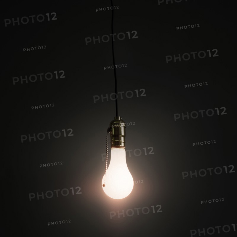 Light bulb hanging against grey background.