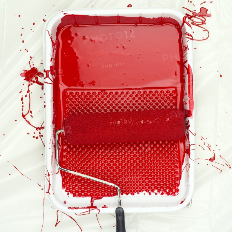 Paint roller on tray with red paint.