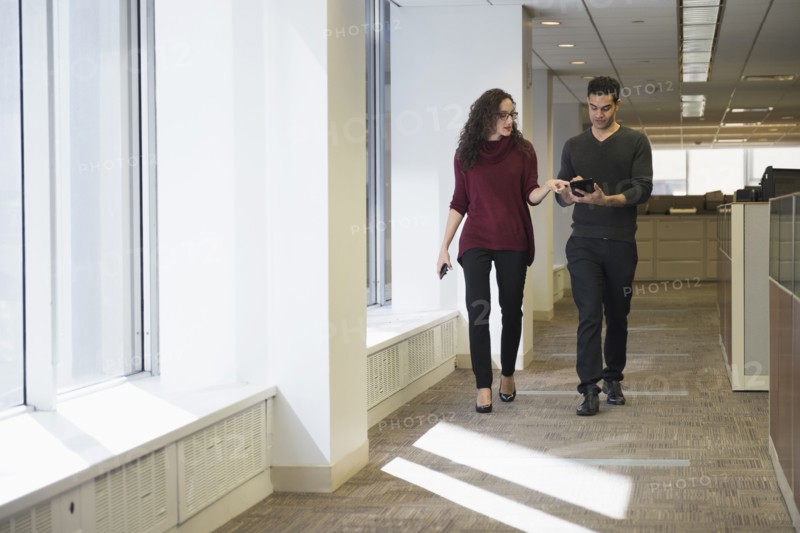 Young people walking side by side in corridor with digital tablet.