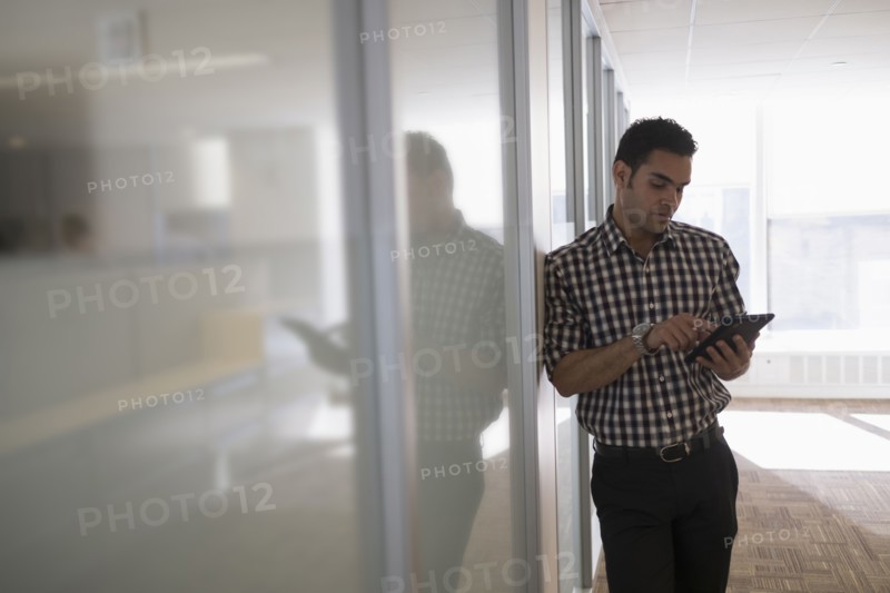 Young man standing in corridor with digital tablet.