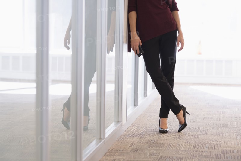Low section of young woman leaning on glass wall.