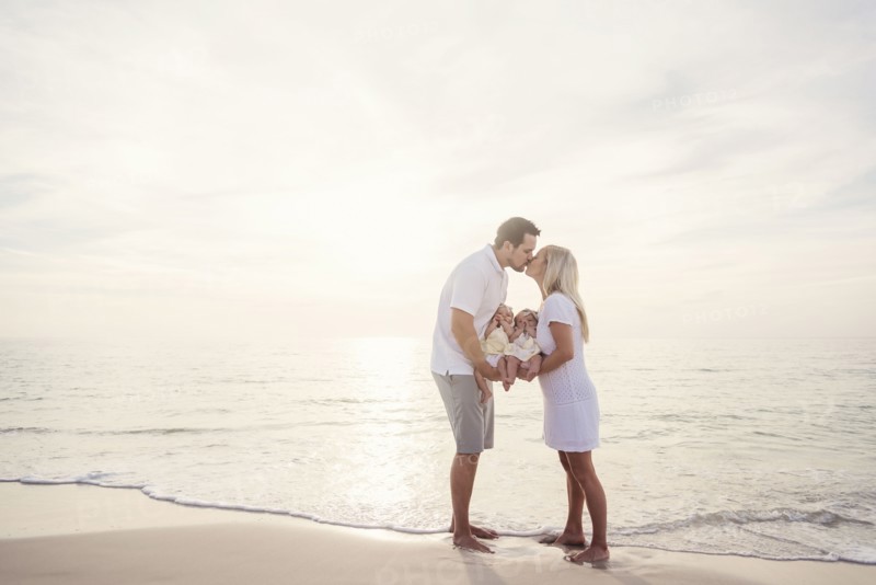 Couple with twins (2-5 months) kissing on seashore