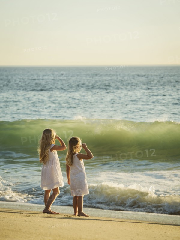 Girls (4-5, 6-7) standing on beach and looking at sea