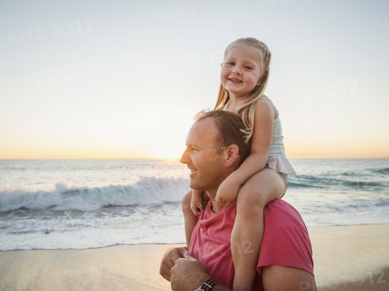 Father carrying daughter (4-5) on beach