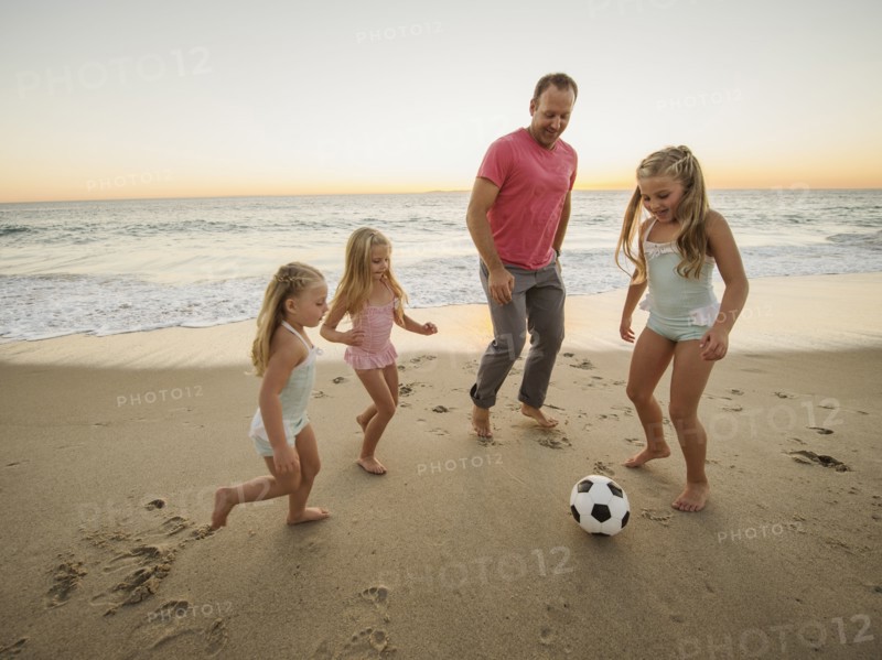 Father with children (4-5, 6-7, 8-9) playing soccer on beach