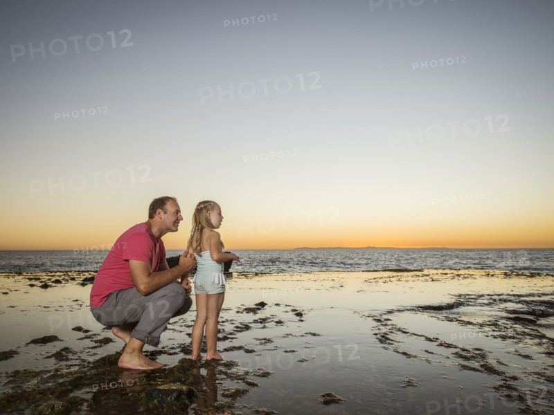 Father crouching next to daughter (4-5) on beach