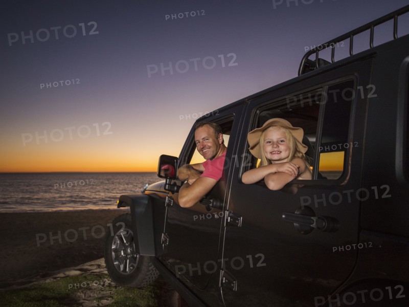 Father and daughter (4-5) sitting in car on beach