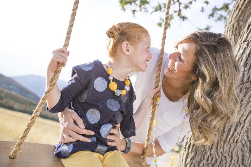 Mother with girl (4-5) sitting on swing