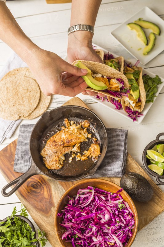 Woman preparing tortilla with tilapia, avocado and red cabbage