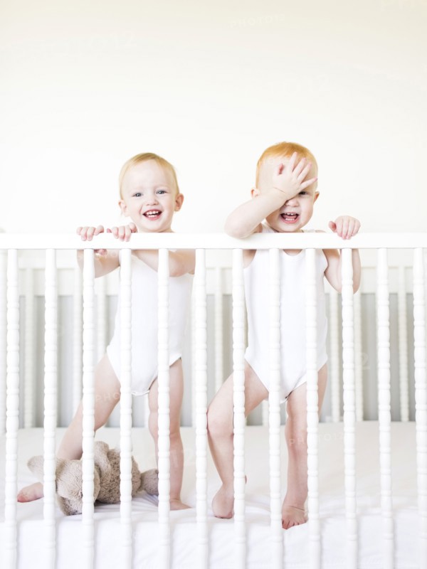 Twin brothers (12-17 months) standing in crib