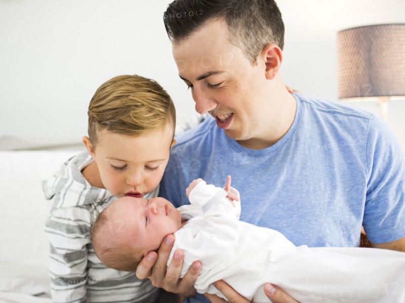 Father carrying daughter (0-1 months) and sitting on bed with son (4-5)
