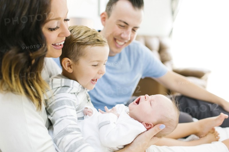 Parents sitting with daughter(0-1 months) and son (4-5) on bed in bedroom
