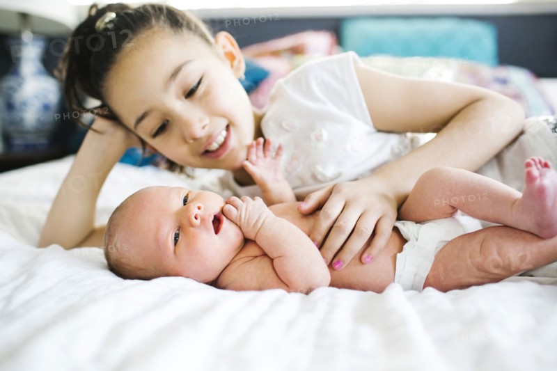Girl (10-11) lying in bed beside brother (2-5 months)