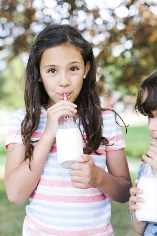 Girl (10-11) and boy (6-7)   in park drinking milk