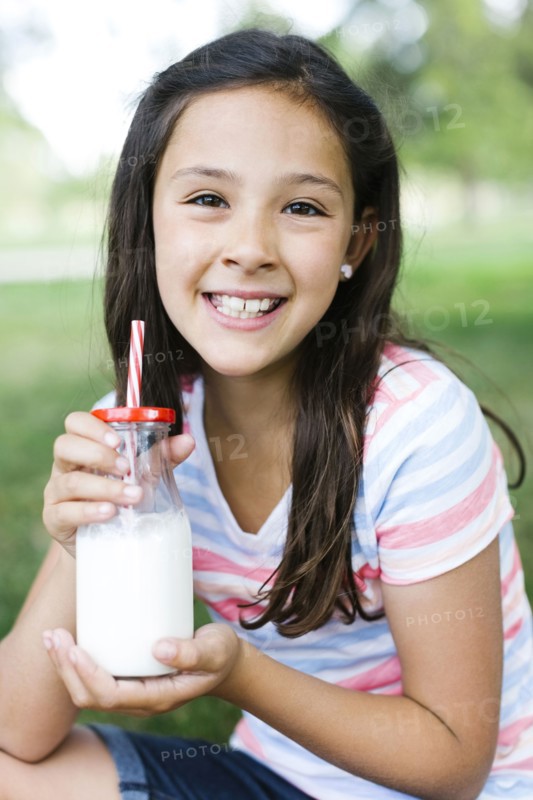 Girl (10-11) in park holding glass of milk with straw