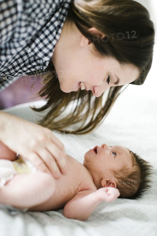 Young mother with baby girl (0-1 months) lying on bed