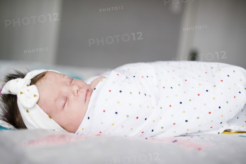 Baby girl (0-1 months) wrapped in blanket sleeping on bed
