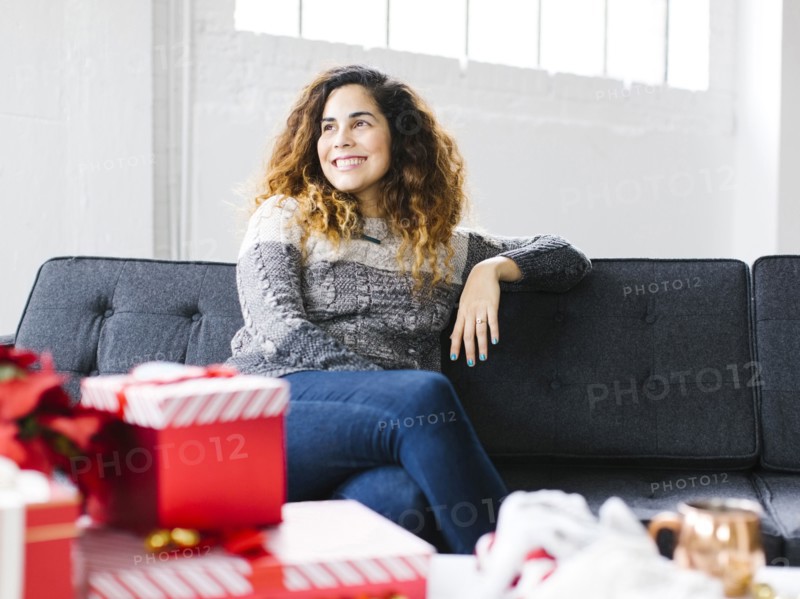 Happy woman on sofa with Christmas gifts in foreground