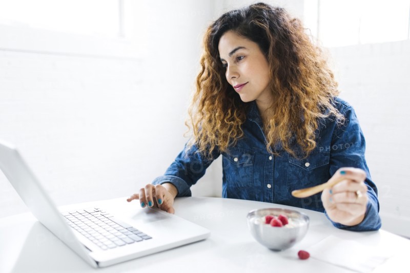 Woman using laptop and eating yoghurt