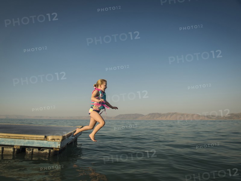 Girl (4-5) jumping into lake from pier