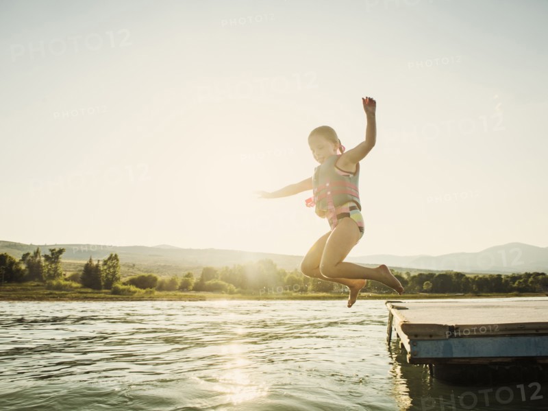 Girl (4-5) jumping into lake from pier