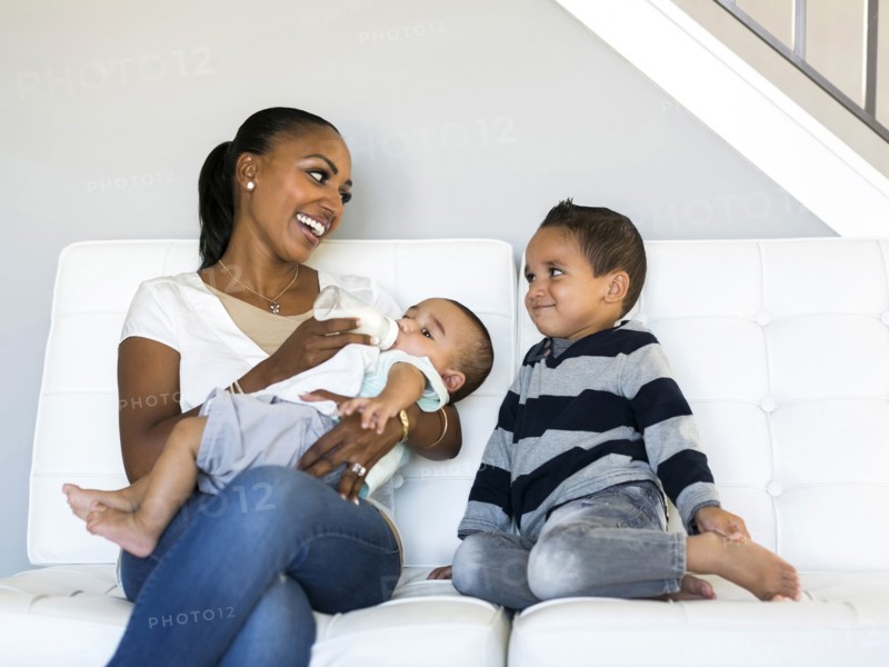 Mother with two sons (2-5 months, 2-3) on sofa