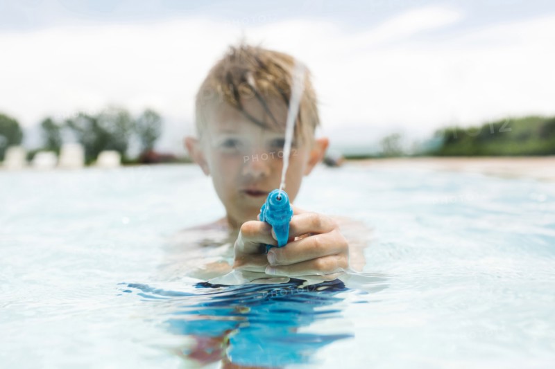 Boy (6-7) playing with squirt gun in swimming pool