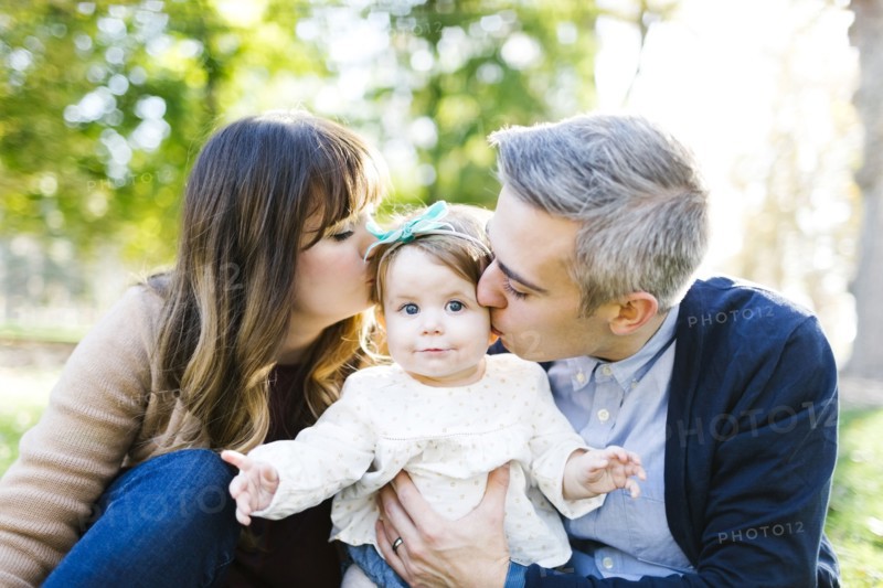 Portrait of parents kissing daughter (12-17 months) in park