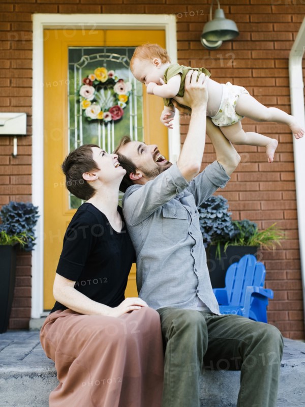 Parents with daughter (12-17 months) sitting in front of house