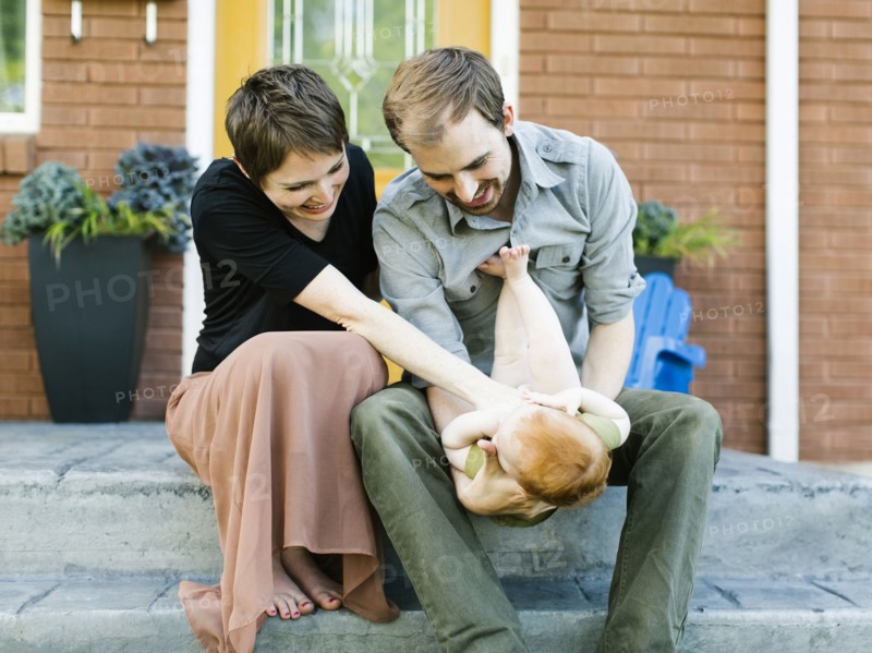 Parents with daughter (12-17 months) sitting in front of house