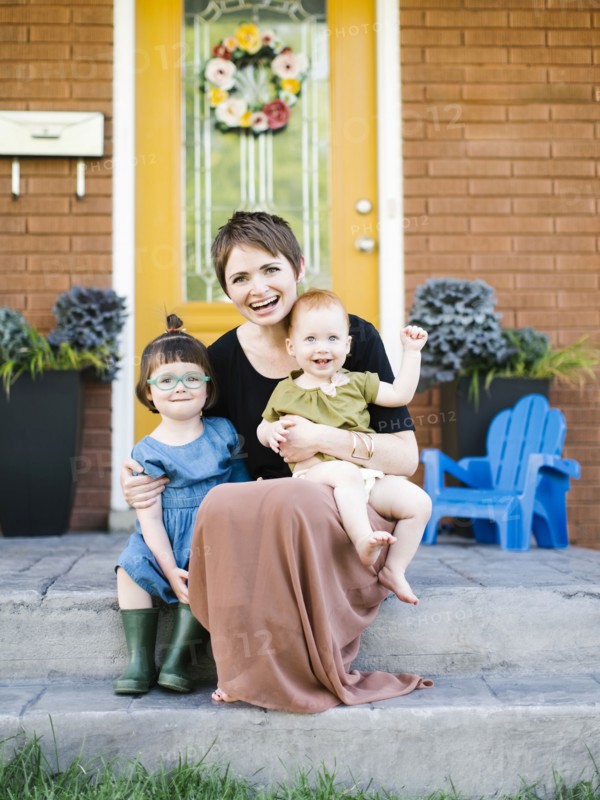 Mother with daughters (2-3, 12-17 months) sitting in front of house