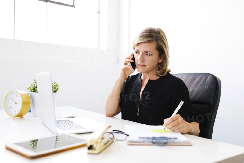 Woman using mobile phone, looking at laptop