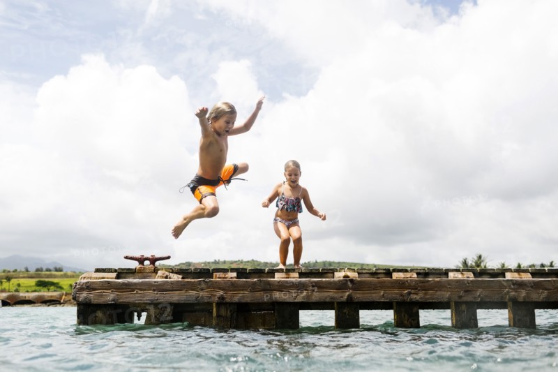 Boy (8-9) and girl (6-7) jumping into sea from jetty