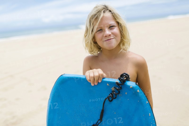 Boy (8-9) standing on beach and holding surfboard