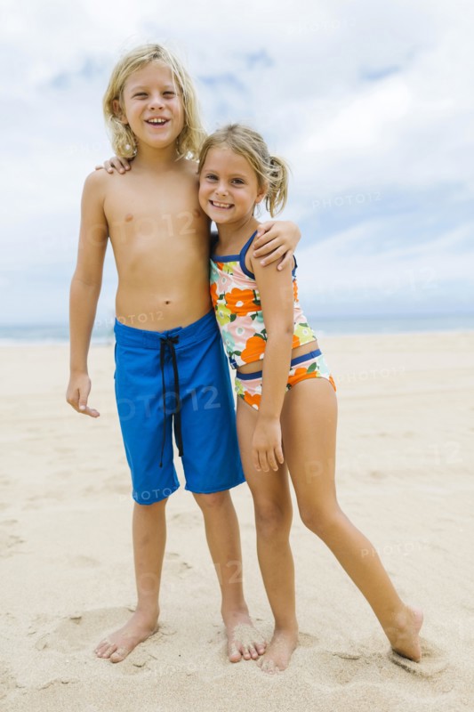 Brother (8-9) and sister (6-7) embracing on beach