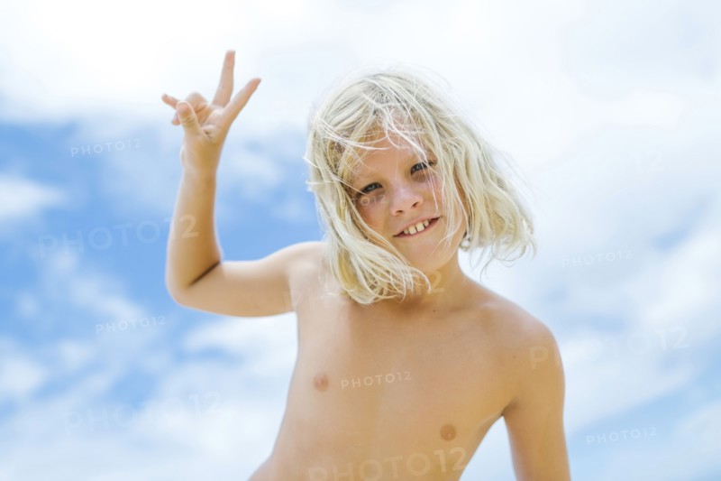 Boy (8-9) showing peace sign against blue sky