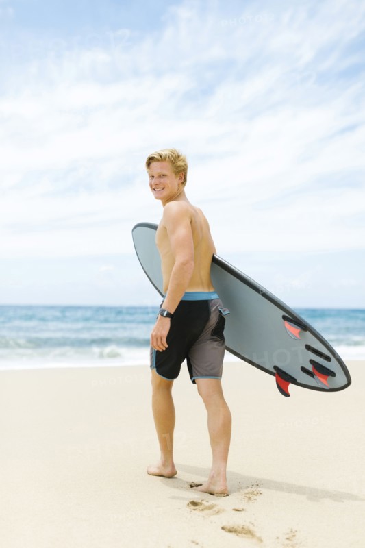 Man walking on beach and holding surfboard