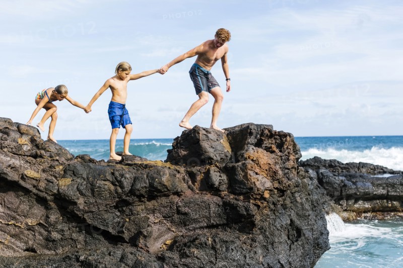 Man and children (6-7, 8-9) walking on rock by sea