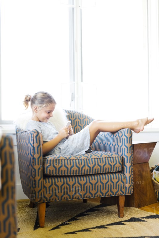 Young girl (6-7) sitting on armchair and using mobile phone