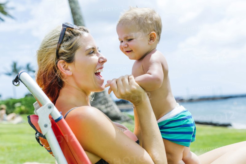Woman sitting under palm tree with little son (18-23 months)