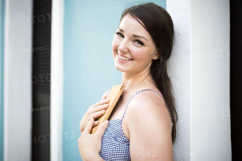 Cheerful woman with digital tablet leaning against building wall