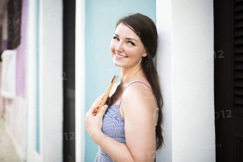 Cheerful woman with digital tablet leaning against building wall