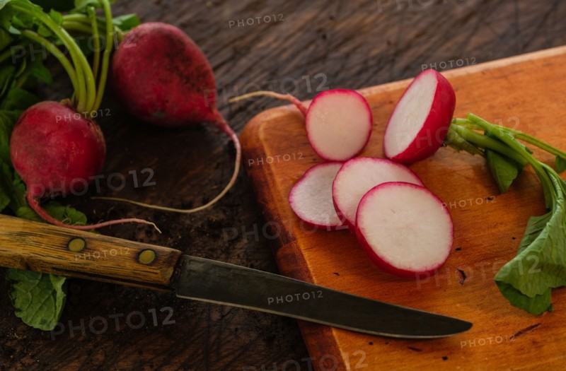 Slices of red radish and knife on cutting board