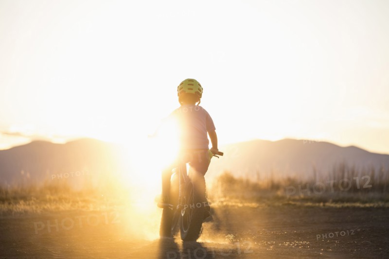 USA, Colorado, Rear view of boy (8-9) cycling at sunset