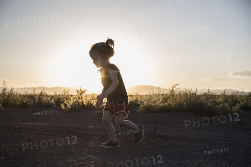 USA, Colorado, Little girl (4-5) running on dirt road at sunset