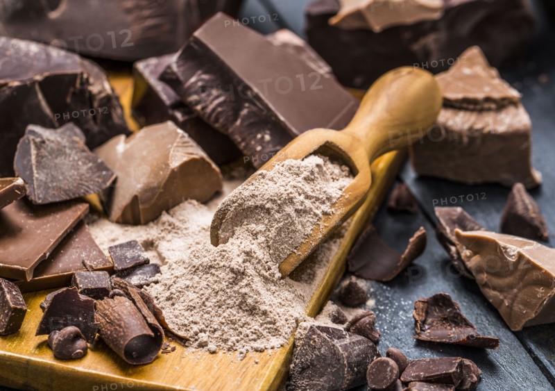 Various pieces of chocolate around wooden scoop with chocolate powder