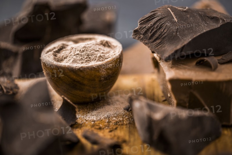 Ground chocolate in wooden bowl next to chunk of chocolate